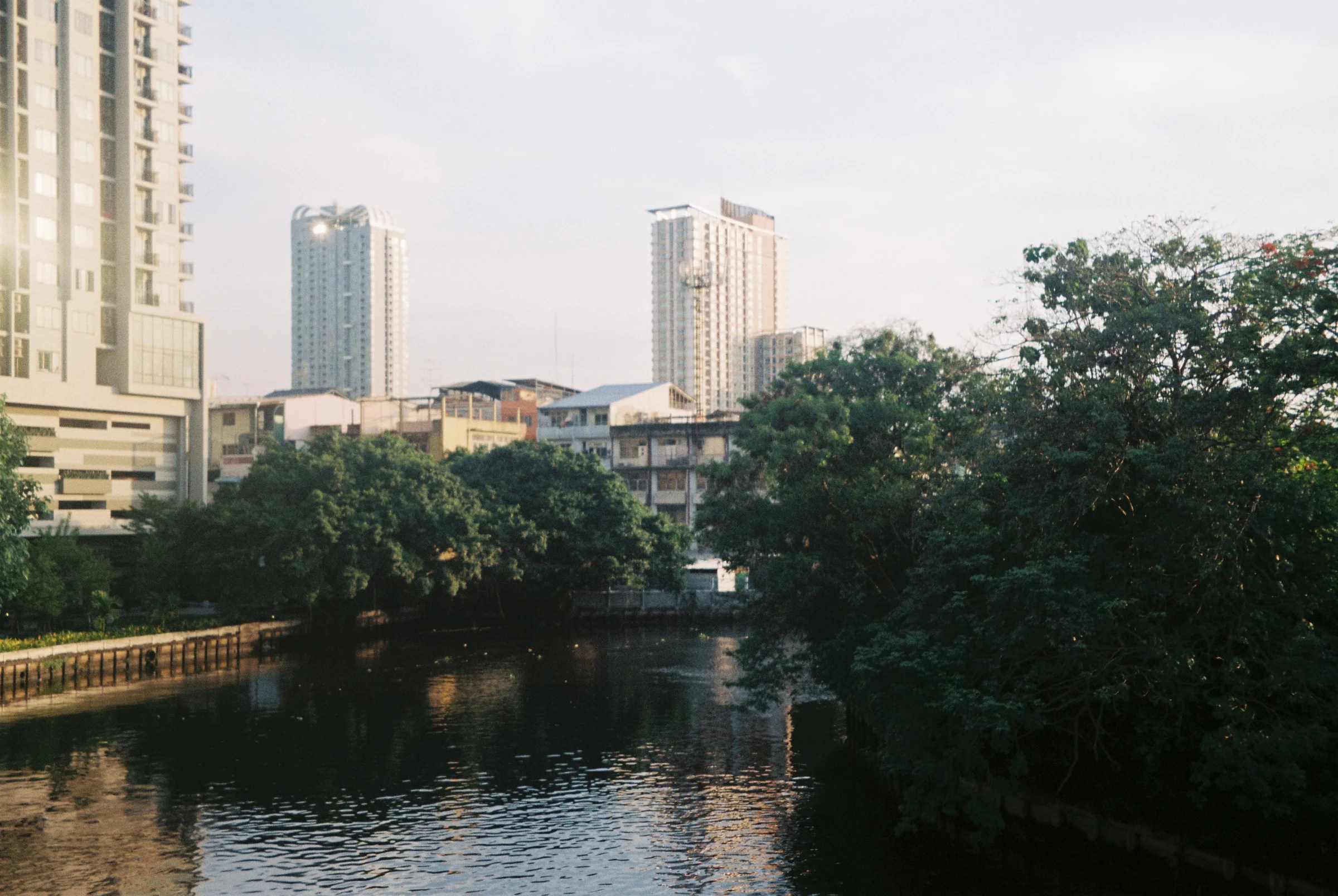 A canal and city buildings in soft evening light in Thailand.