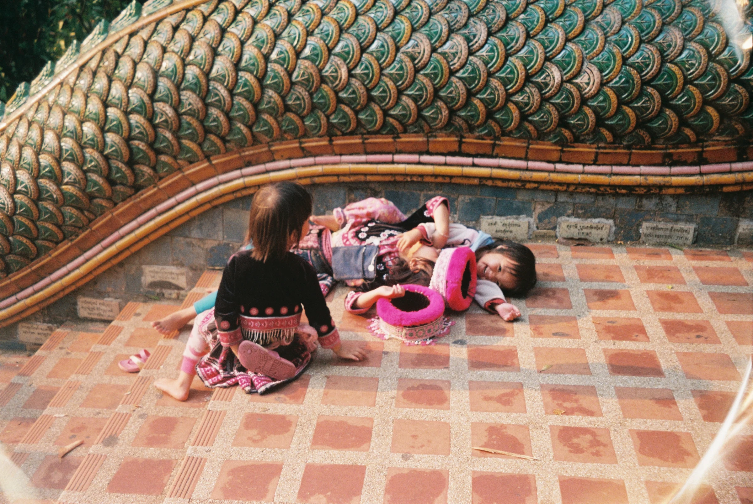 Children resting beside a temple serpent sculpture in Thailand.