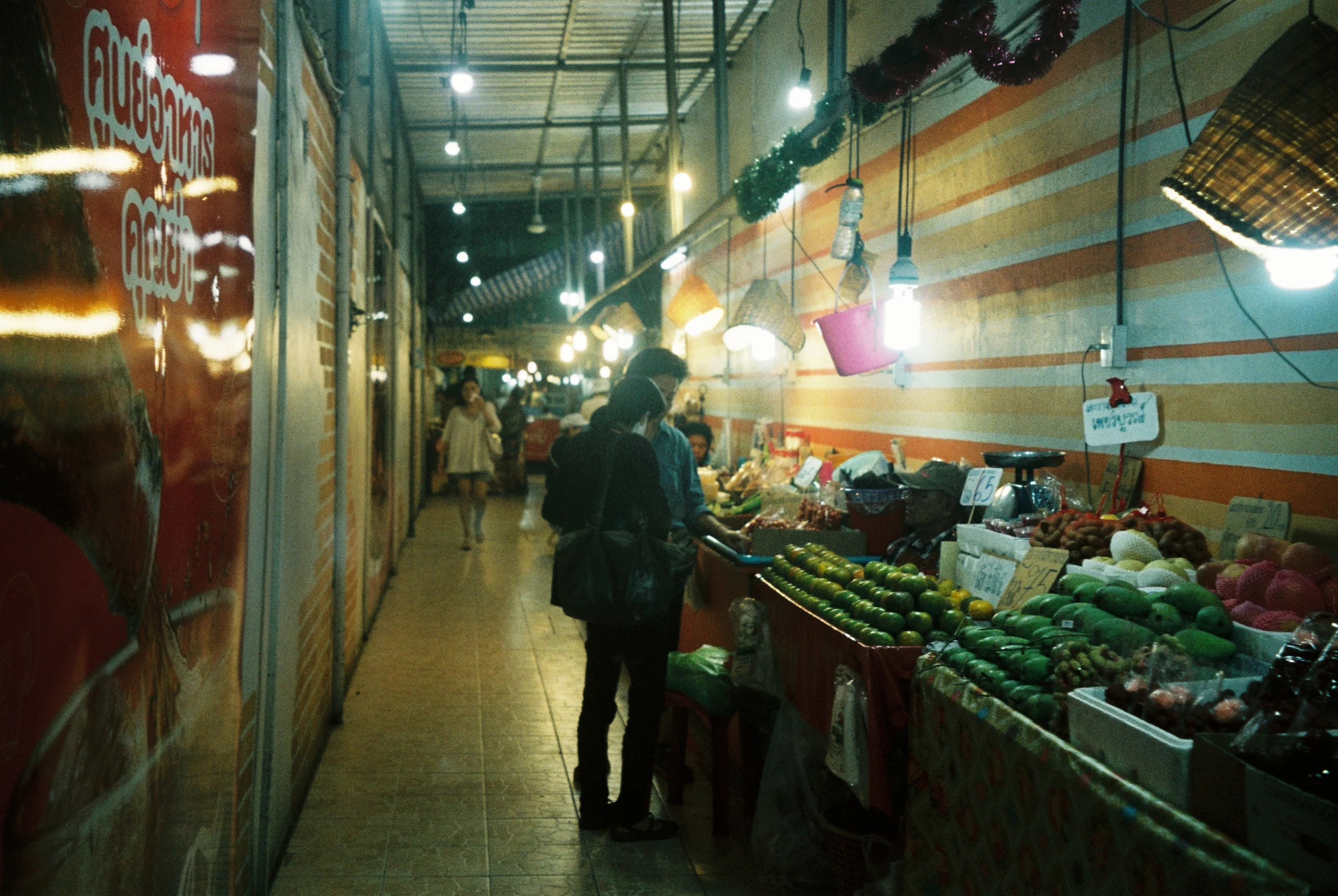 A narrow night market aisle with produce stalls and hanging lights in Thailand.