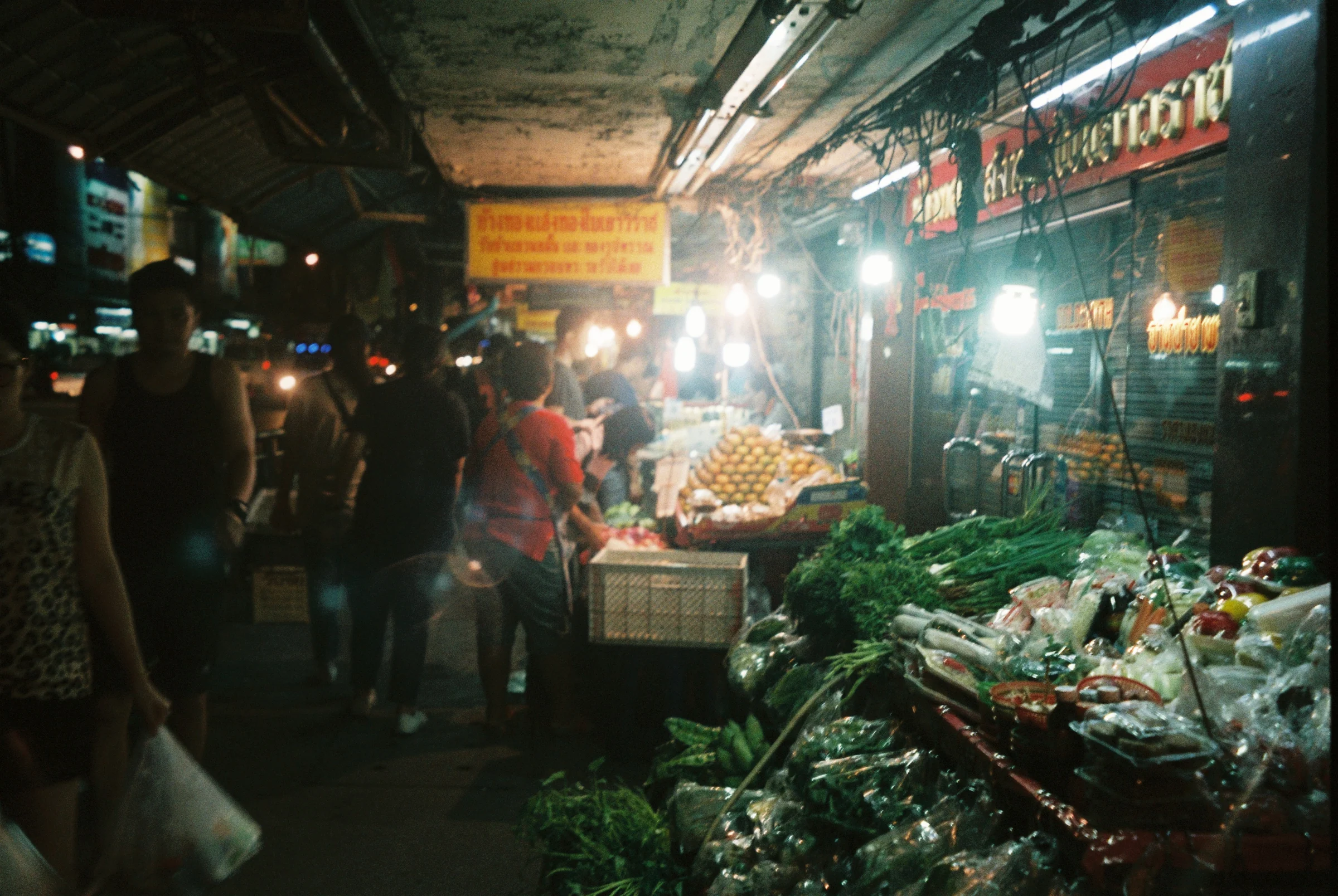 Vegetable stalls glowing under night market lights in Thailand.