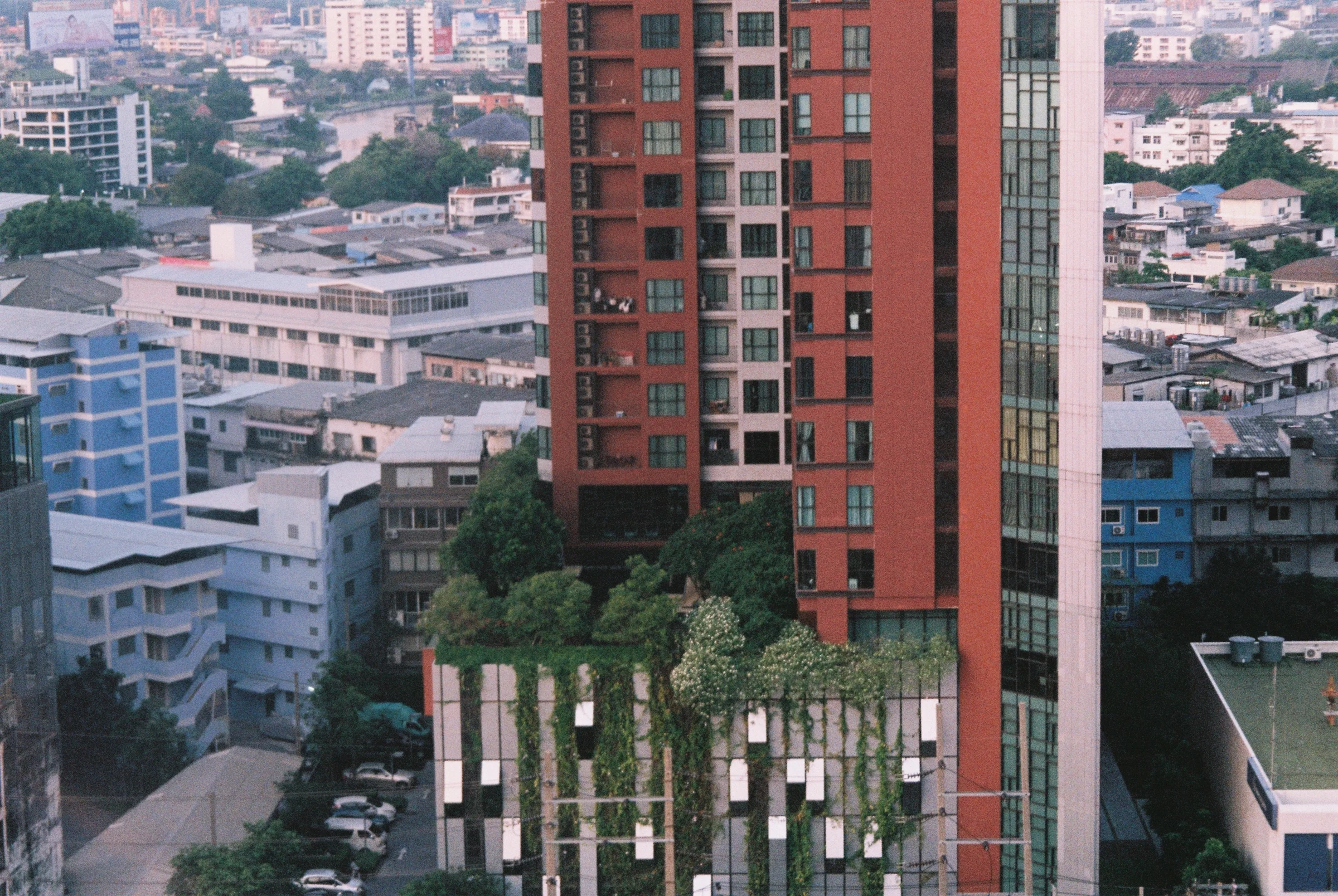 A red residential tower rising over a dense Thai cityscape.